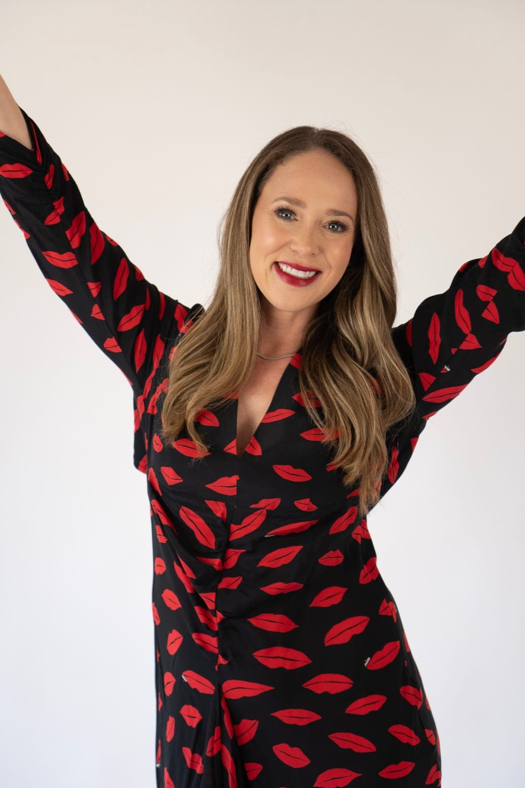 Laura in a lips-print dress with arms raised in celebration